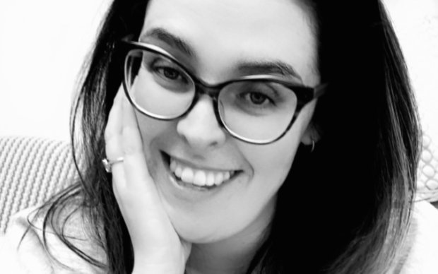 Black and white headshot of Laura smiling. She has long hair and glasses.