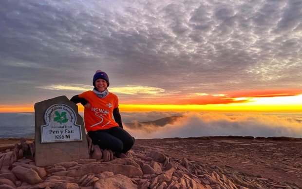 Image shows a woman smiling wearing an orange t shirt at the top of Pen y Fan