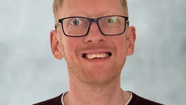 Headshot of Shaun, who has strawberry blonde hair and wears glasses, smiling.