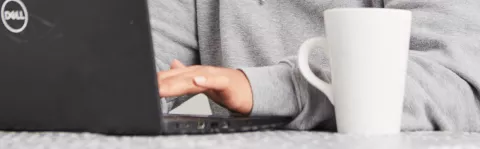 A close up of hands typing on a lap top and a coffee cup