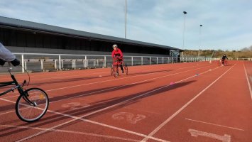 A red sports track with people running using wheeled frames