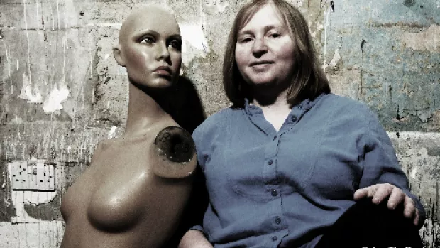 Ann sits resting against a rough concrete wall next to a shop mannequin's torso