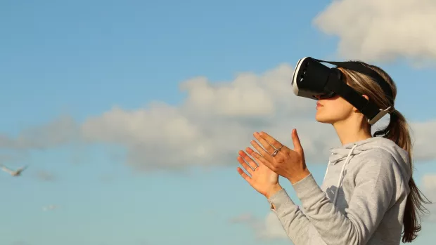 A woman wears a virtual reality headset with her hands out in front of her against a blue sky backround