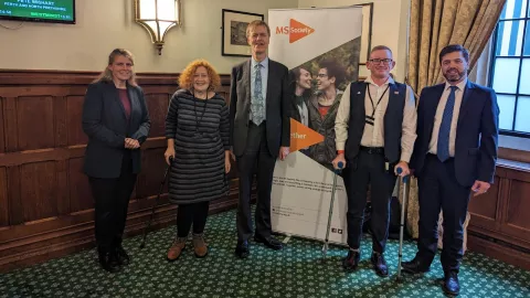The photo shows a group of people standing in-front of an MS Society banner in Parliament