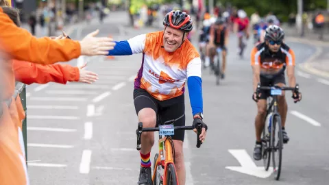 A cyclist in an orange MS cycling shirt high-fives supporters, also wearing orange