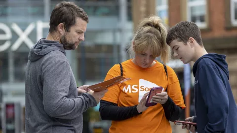 A person in an MS Society t-shirt looks at their phone while another looks on